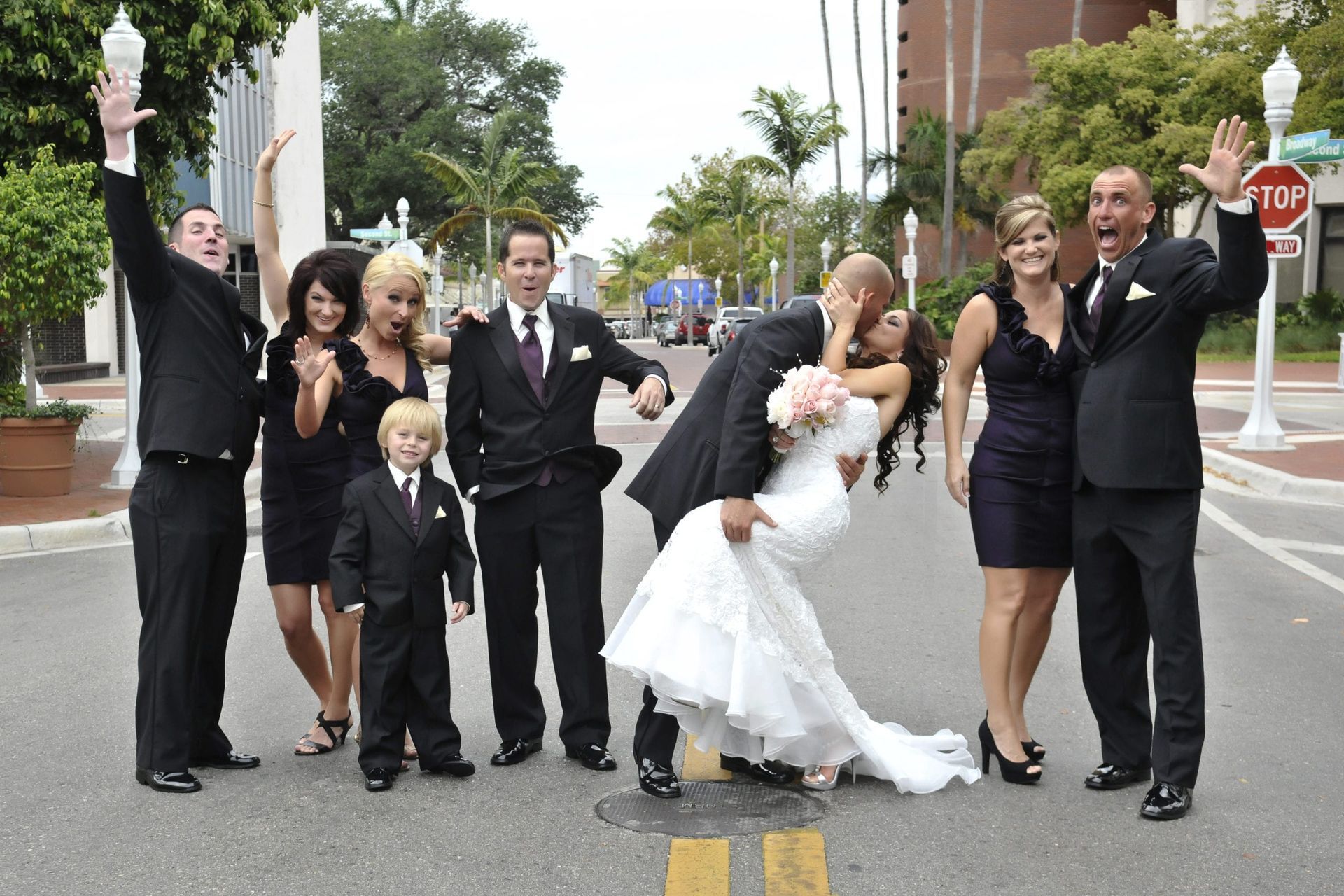 Wedding party in a street: Bride & groom kissing; attendants in formal wear; jubilant expressions.