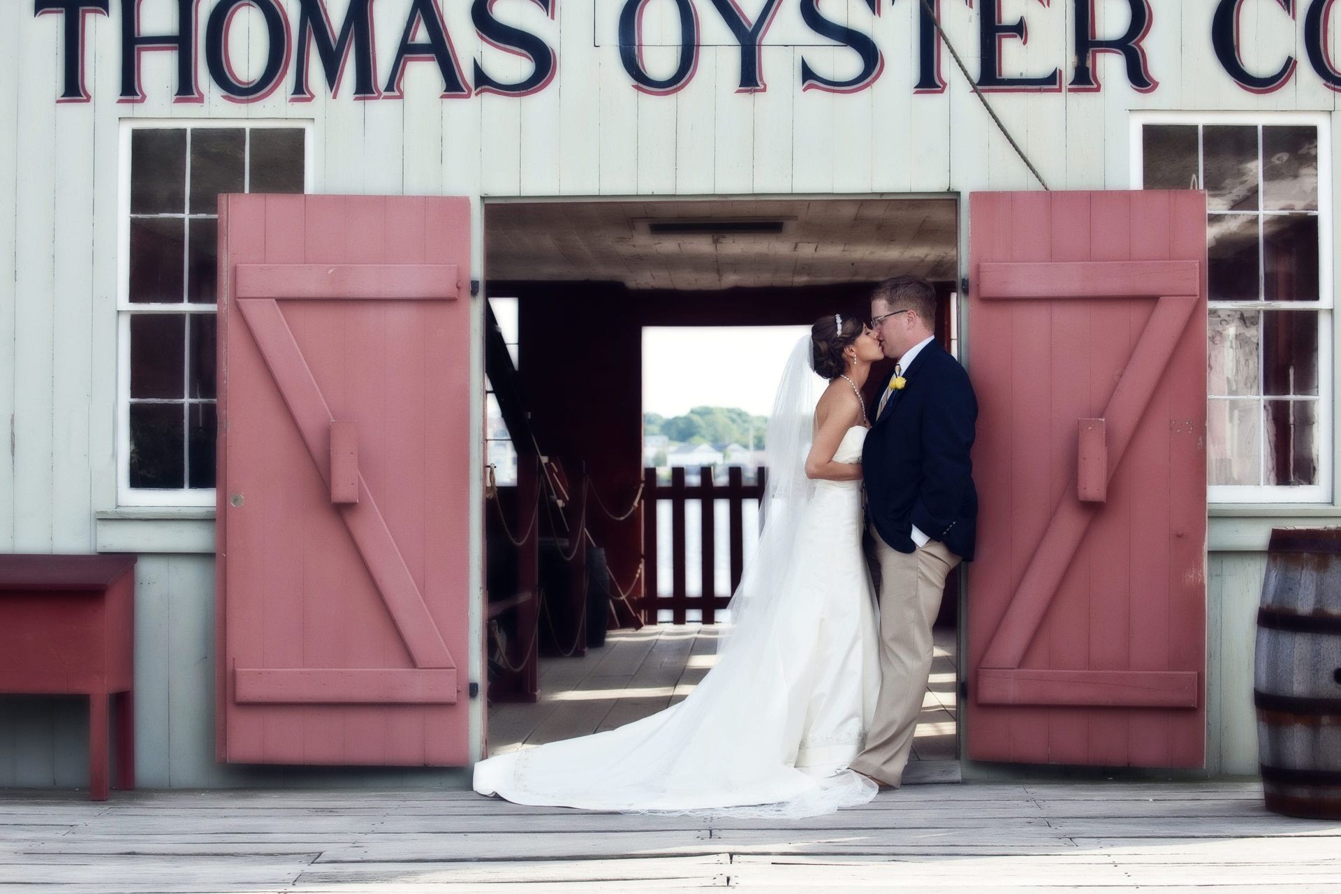 Bride and groom kissing in front of a rustic oyster company building.
