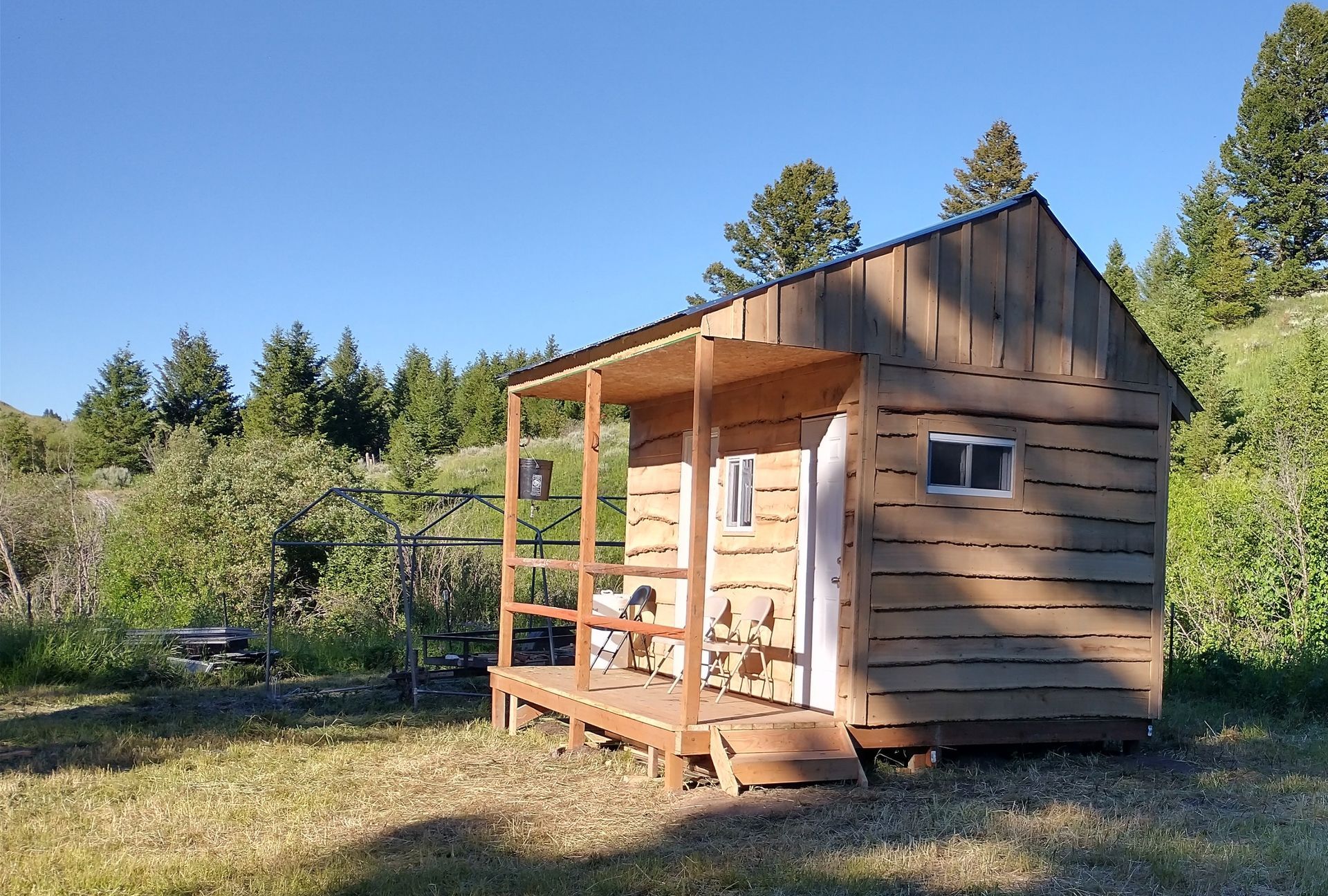 A small wooden cabin with a porch and trees in the background