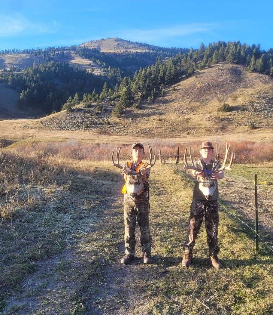 Two men are standing in a field holding deer in their hands.