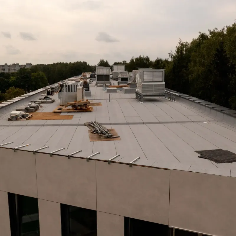 Flat rooftop with HVAC units, scattered materials, and a tree-lined horizon at dusk