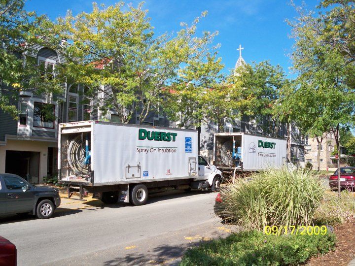 Two Durst moving trucks parked on street in front of buildings and church. Sunny day.