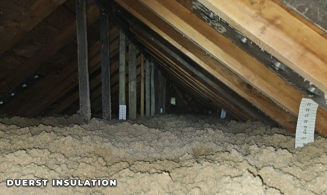 Attic with exposed wooden rafters and cellulose insulation.