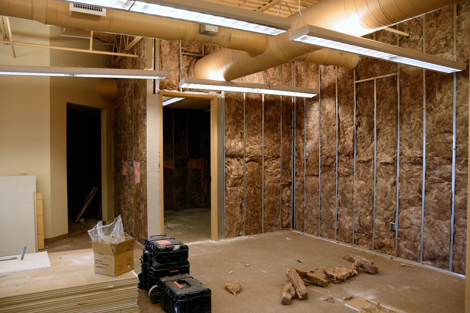 Interior of a room under construction with exposed studs, insulation, and lighting fixtures.