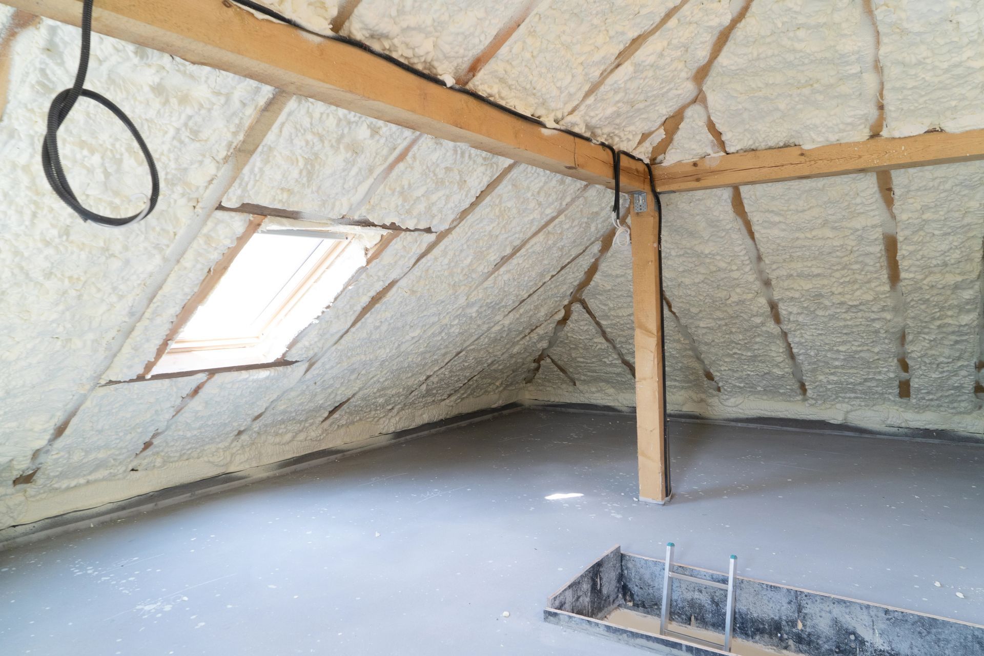 Attic space with spray foam insulation on the angled ceiling, a small skylight, and a concrete floor.