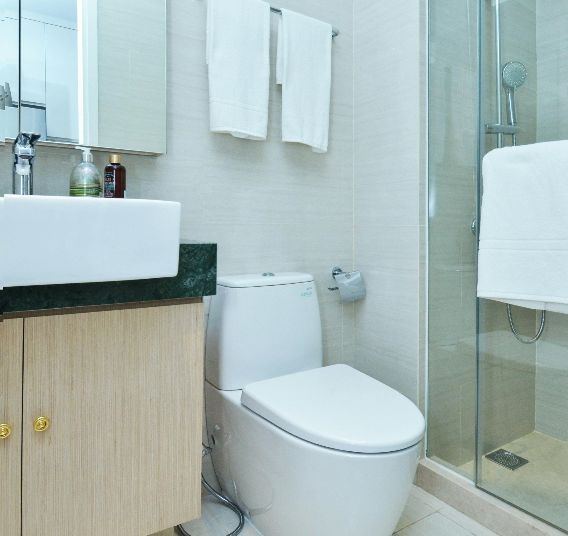 Bathroom with a white toilet, sink, shower, and wooden cabinet with gold knobs. White towels hang.