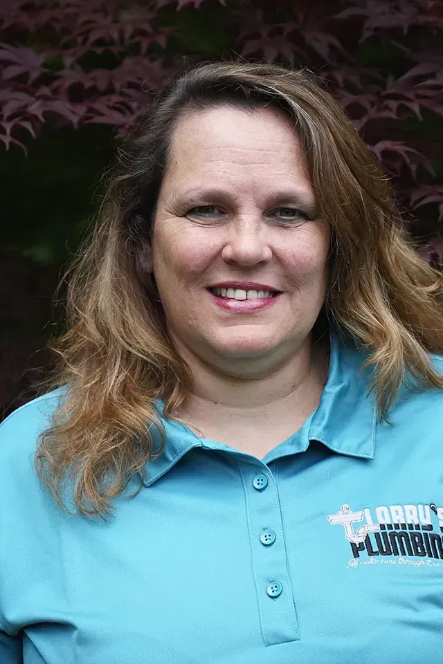 Woman in teal polo shirt smiling, in front of a blurry purple tree.