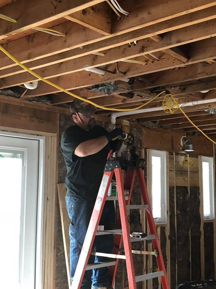 Man on a ladder works on exposed ceiling wiring in a room under construction.