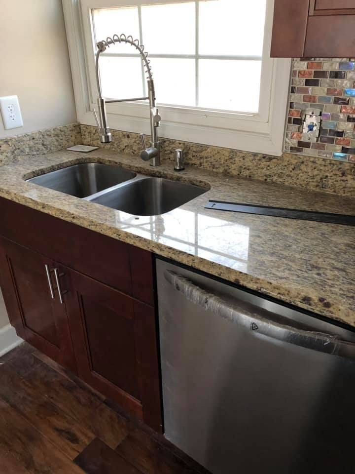 Kitchen with granite countertop, double sink, stainless steel dishwasher, and dark cabinets.