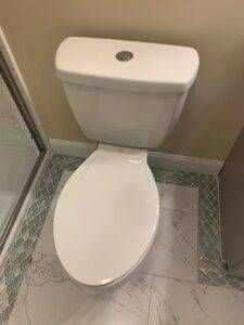 White toilet in a bathroom with tiled floor and wall; glass shower door on the left.
