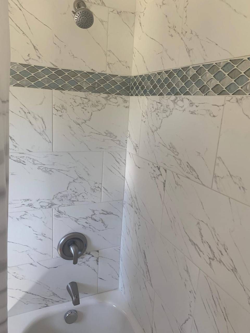 White marble shower with blue tile accent band, chrome fixtures.