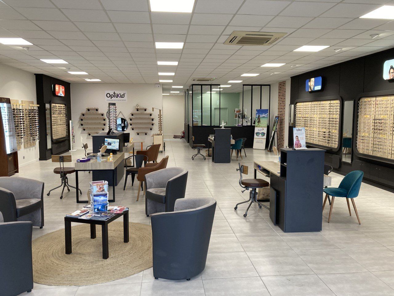 Intérieur d'un magasin de lunettes : présentoirs de montures, sièges et comptoir d'accueil.