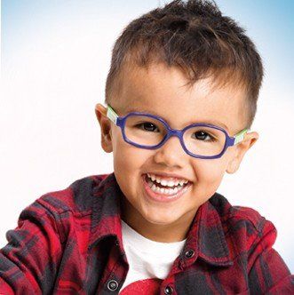 Enfant souriant portant des lunettes bleues et vertes et une chemise à carreaux rouges.