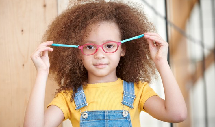 Jeune fille aux cheveux bruns bouclés, portant des lunettes roses et une chemise jaune