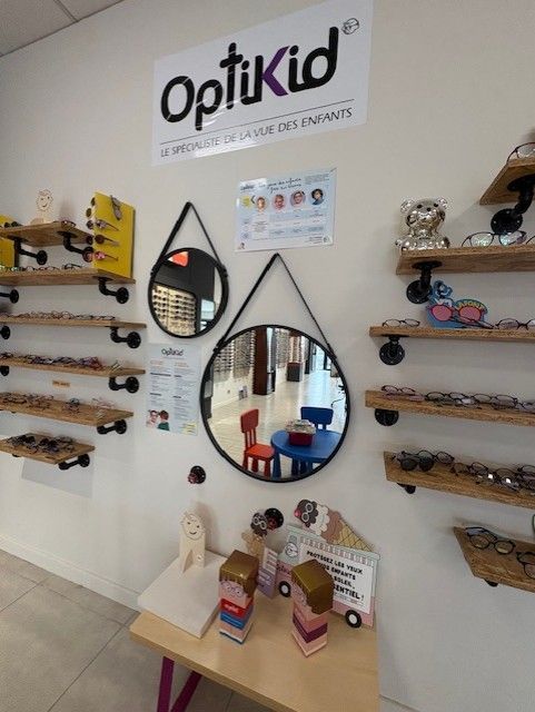 Intérieur du magasin d'optométrie pour enfants OptiKid, avec présentoirs à lunettes, miroirs ronds et table pour enfants.