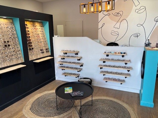 Intérieur d'un magasin d'optique avec présentoirs à lunettes, comptoir d'accueil et décorations murales.