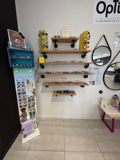 Présentoir de magasin d'optique avec des lunettes sur des étagères en bois, deux miroirs ronds et des affiches colorées.