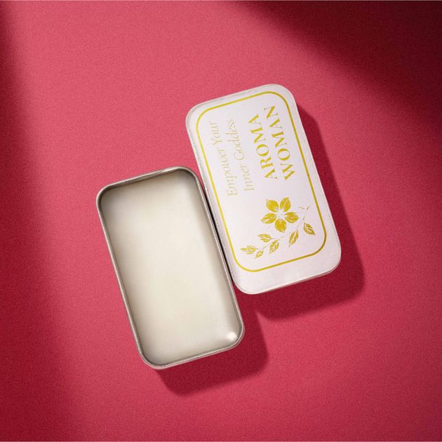 打開的金屬罐裝「AROMA WOMAN」香水放在粉紅色的表面上。