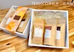 木桌上放著兩個茶葉禮盒。每個盒子裡都裝著一個用牛皮紙包裹的茶包，其中一個茶包的外包裝上有一個花紋。