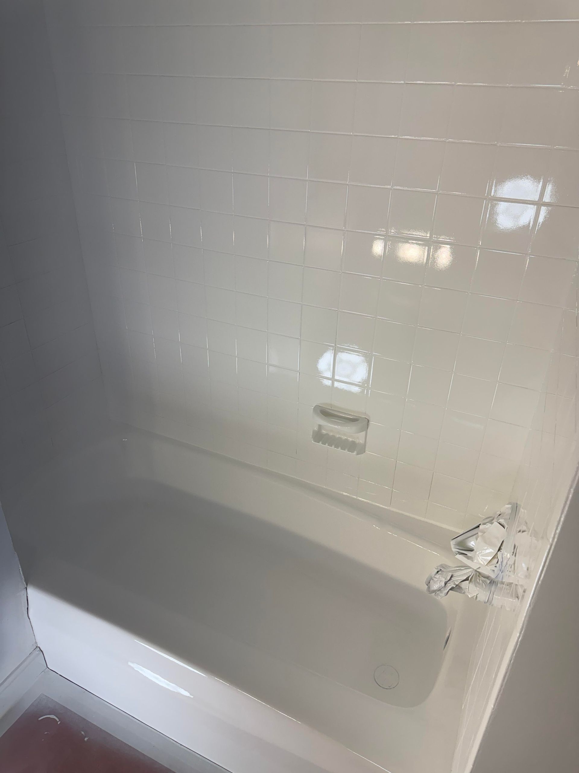 White bathtub and tiled shower wall with built-in soap shelf and chrome fixtures.