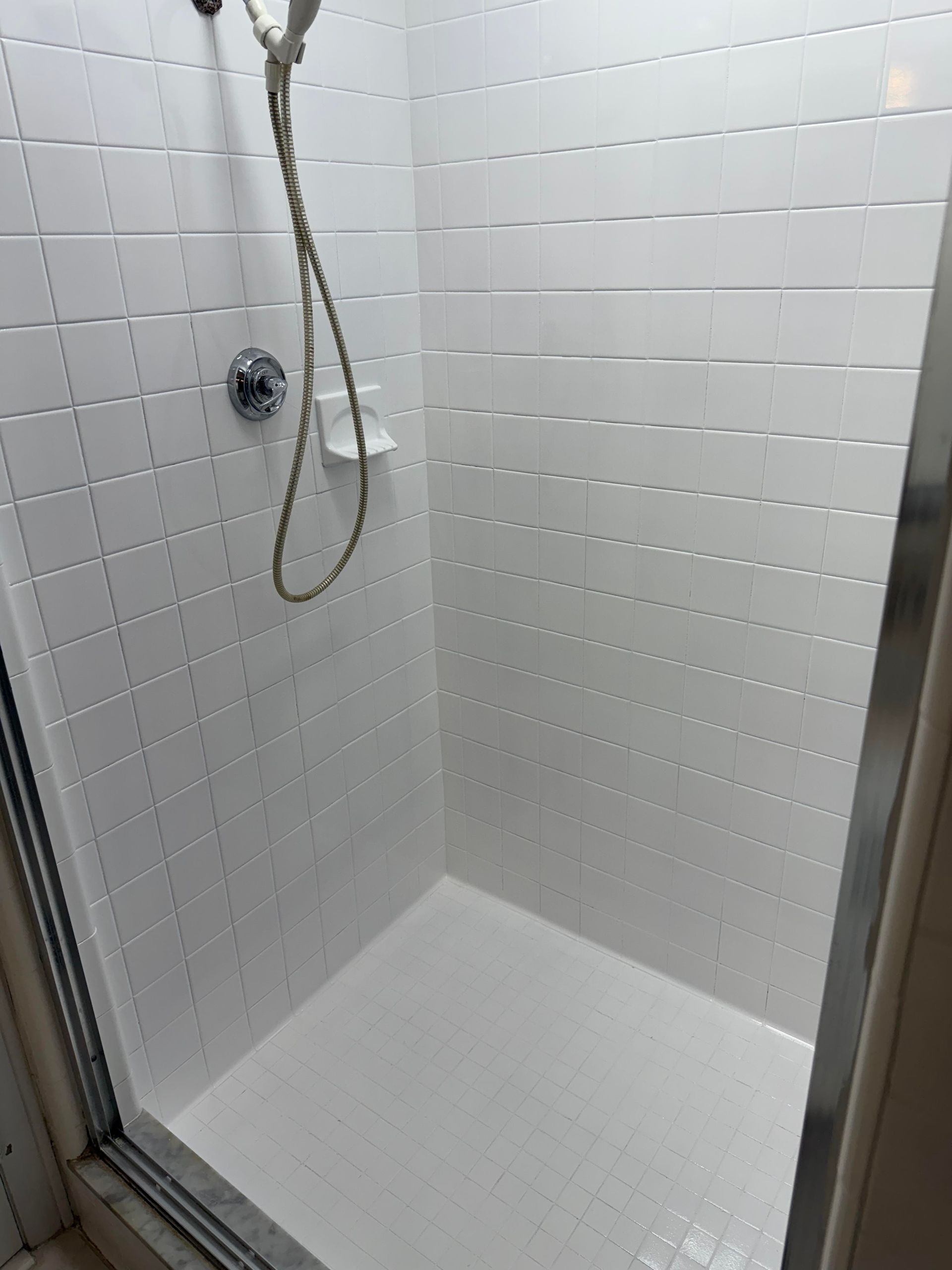 Empty white tiled shower stall with a handheld shower and drain