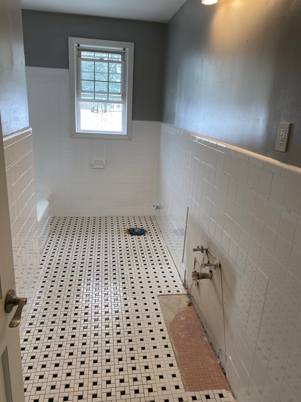 Bathroom with black and white tiled floor, white tiled walls, and a window.
