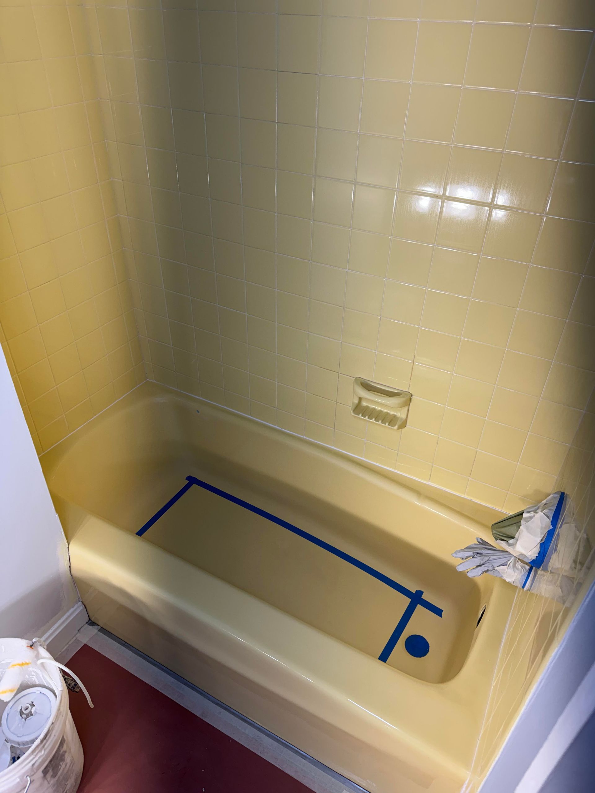 Yellow-tiled bathtub with blue tape marking the floor and a small repair patch on the wall