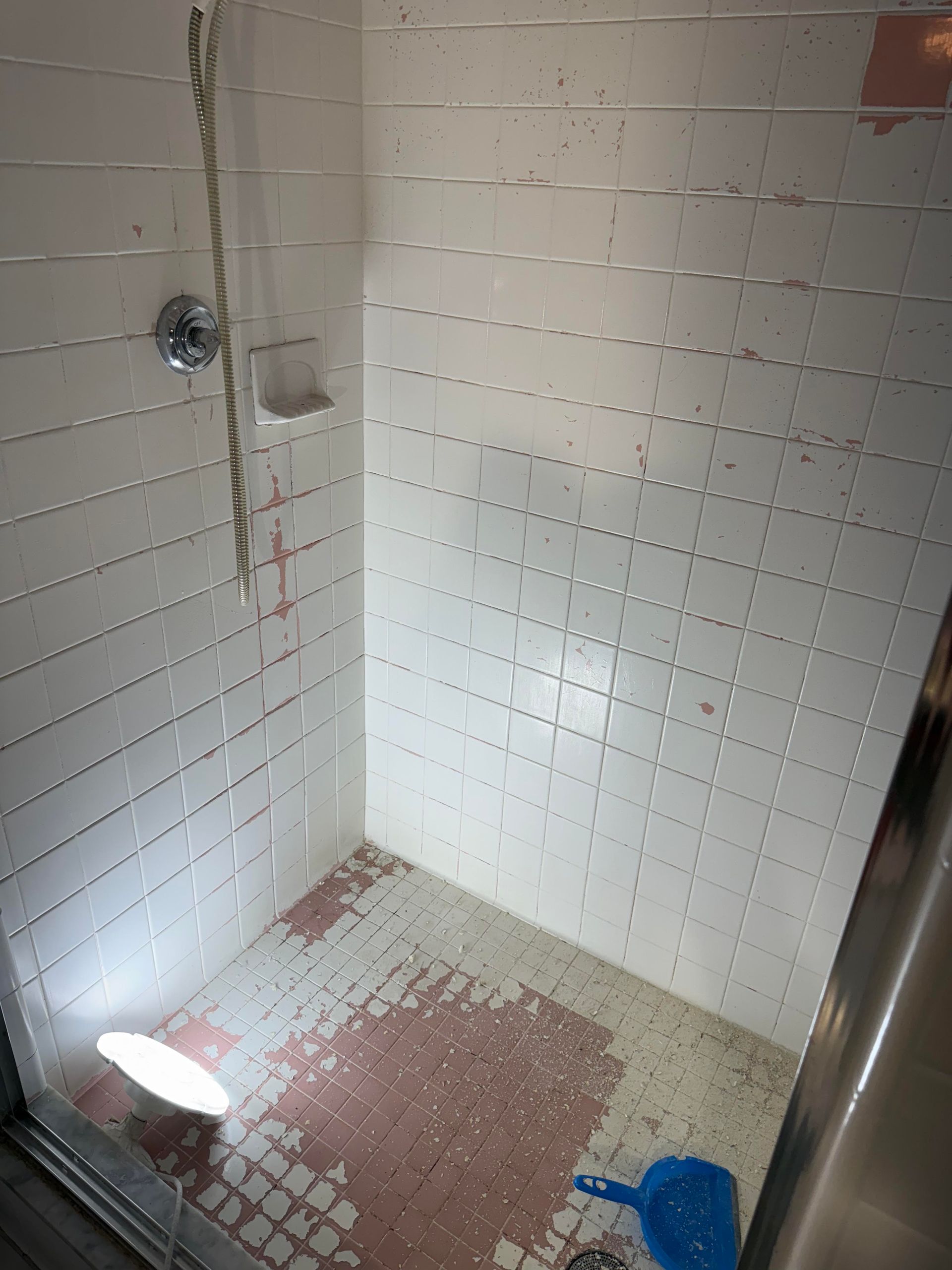 Tiled shower stall with a showerhead, drain, and cleaning supplies on the floor.