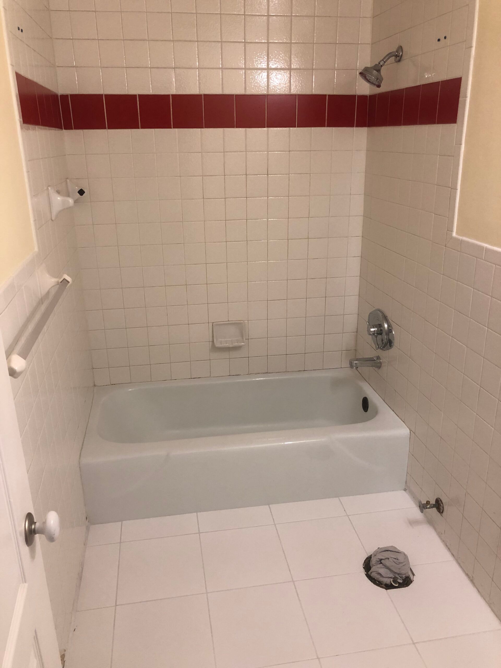 White bathroom with red trim, white tub, and white tiled walls and floor.