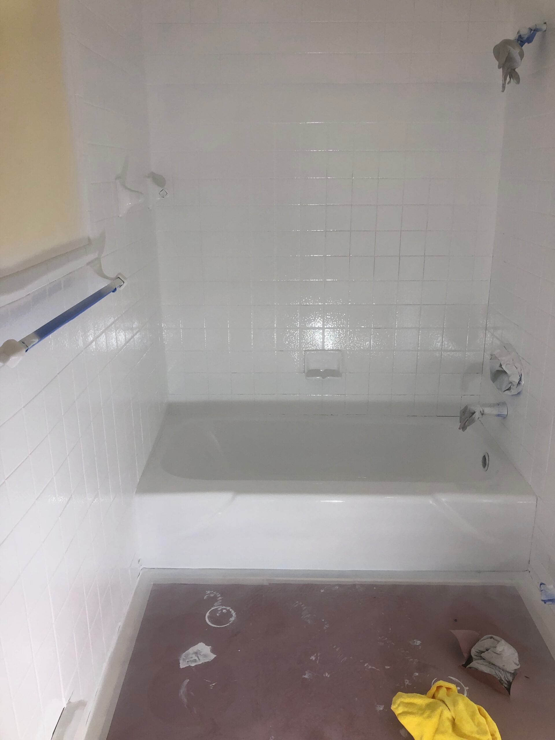 White tiled bathroom with a bathtub and red-brown floor. Spray paint is visible.