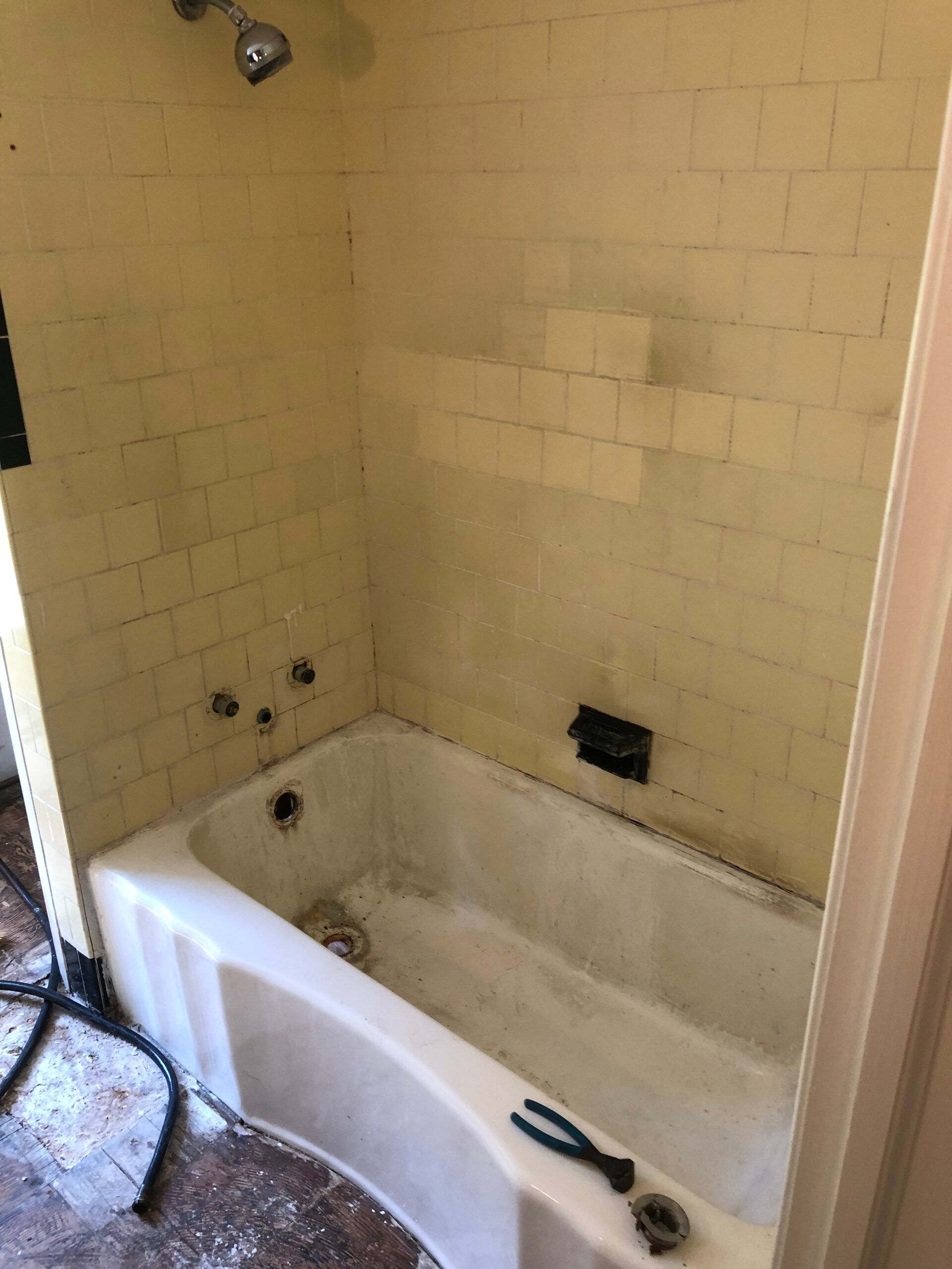 Yellow tiled bathtub and shower with chrome fixtures. Pliers and pipe fittings sit on the tub edge.