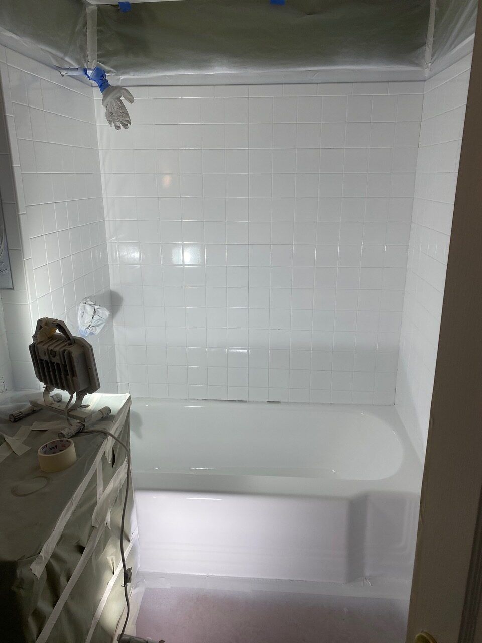 A white-tiled bathtub enclosure under construction, with taped-off fixtures and a light in a bathroom.
