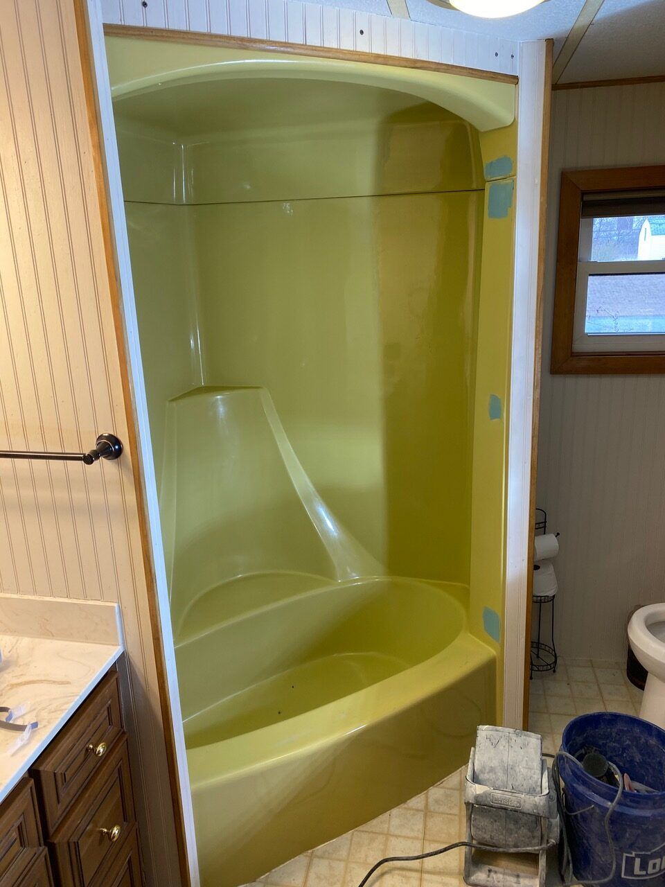 Yellow one-piece bathtub and shower combo, under construction. The room is partially finished with wallpaper and wood trim.