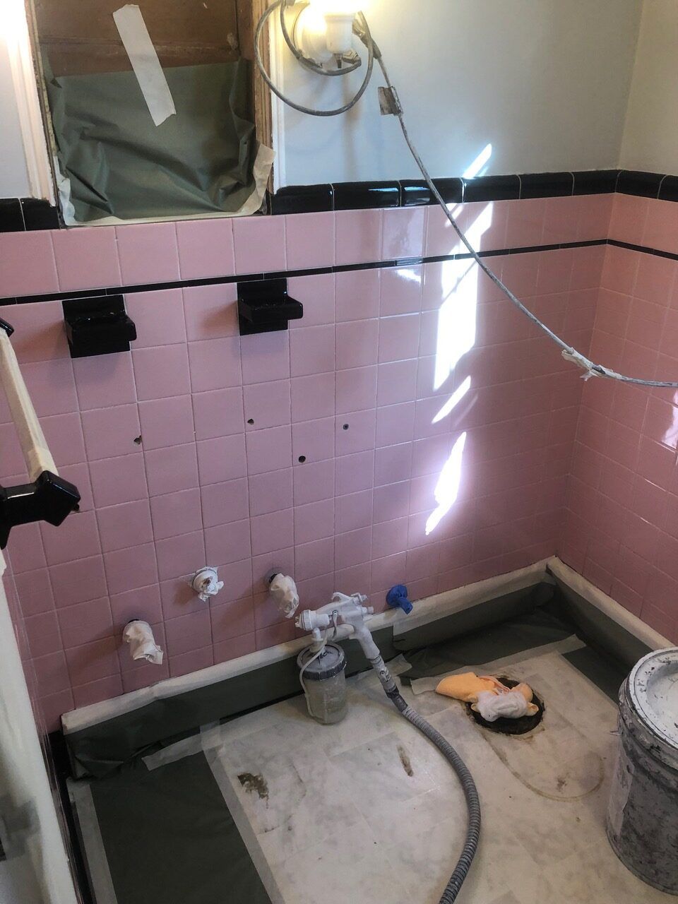 Pink tiled bathroom under renovation, with black trim, exposed plumbing and wires.