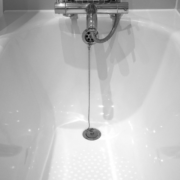 Close-up of a bathtub drain with a metal pull cord in a white tub.
