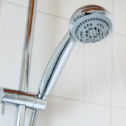 Chrome shower head with water spraying, in a tiled shower.