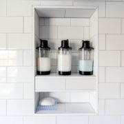 White tiled shower niche holding three soap dispensers and a soap bar on a brush.