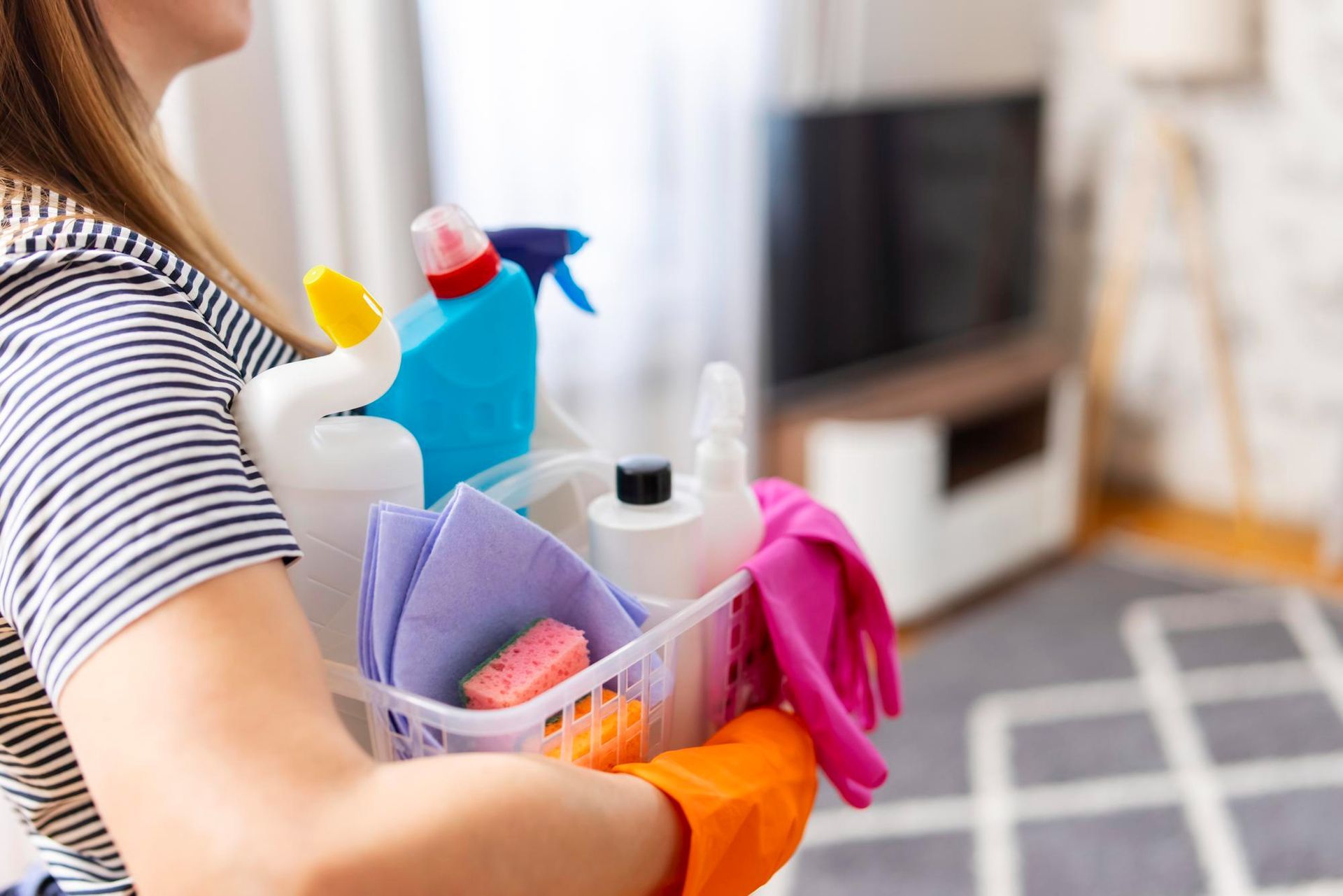 A woman is holding a basket of cleaning supplies in a living room.