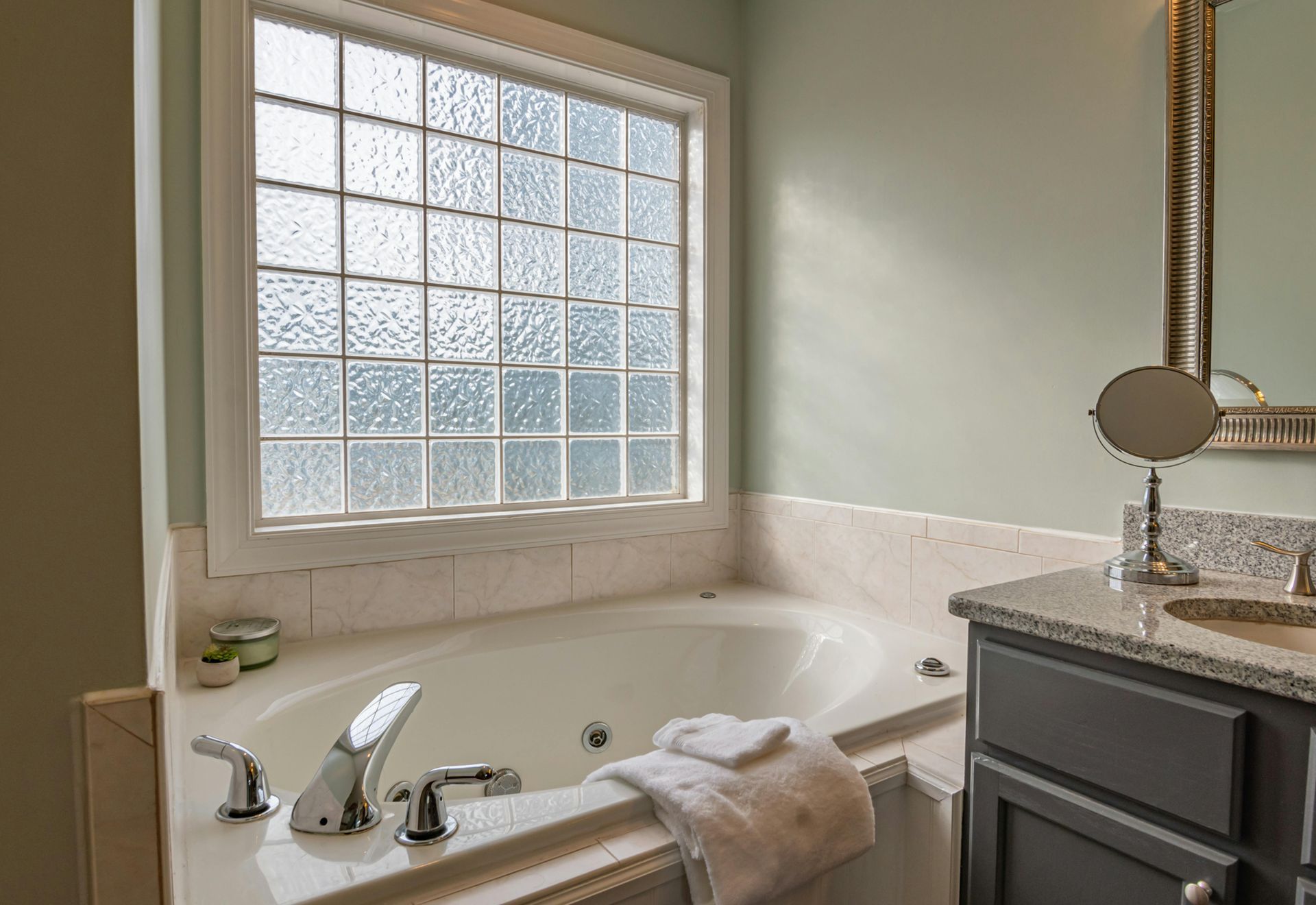 Bathroom with a jetted tub, window with textured glass, and a vanity with a mirror.