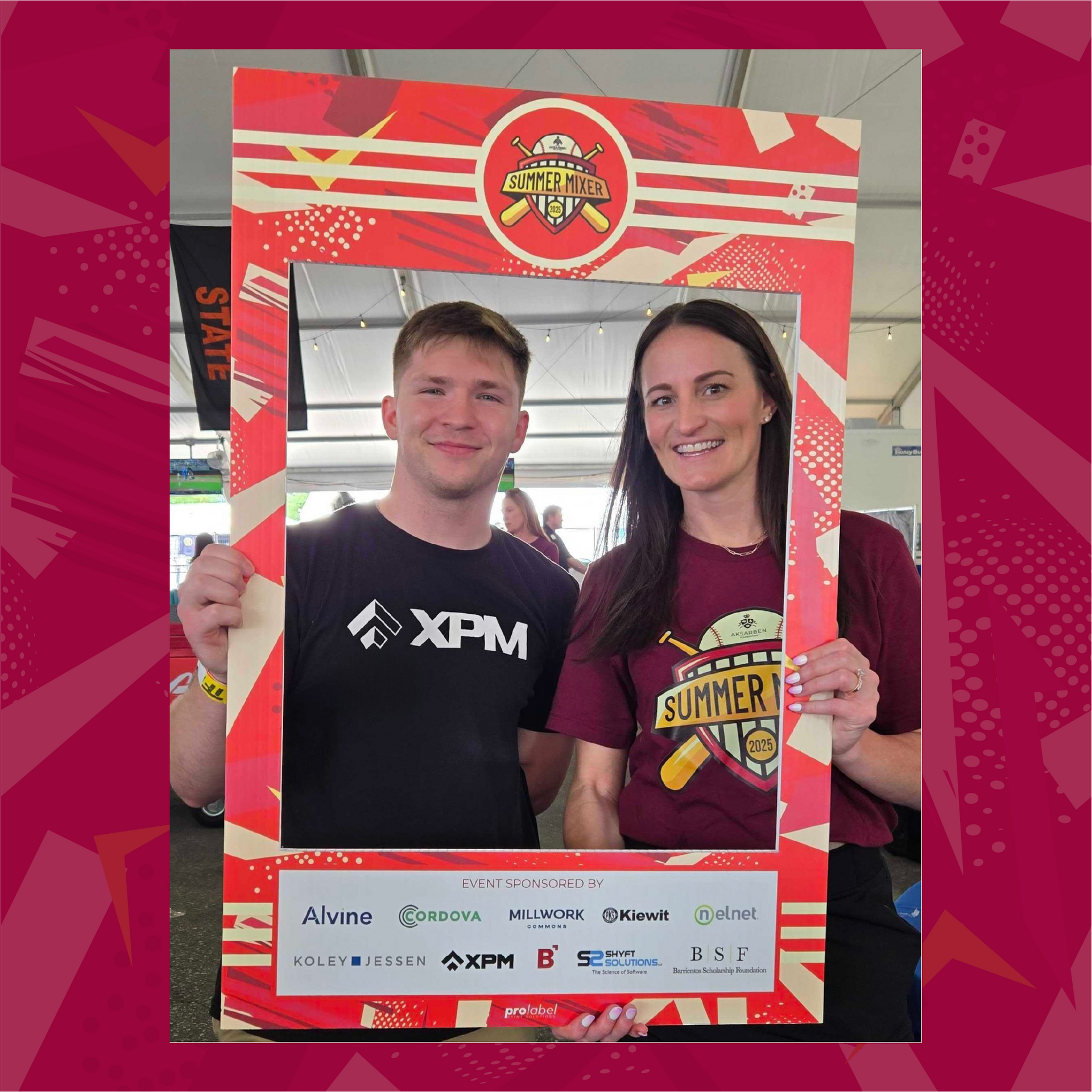 Two people in a photo booth frame. Man wears black shirt, woman wears maroon shirt. Baseball event.