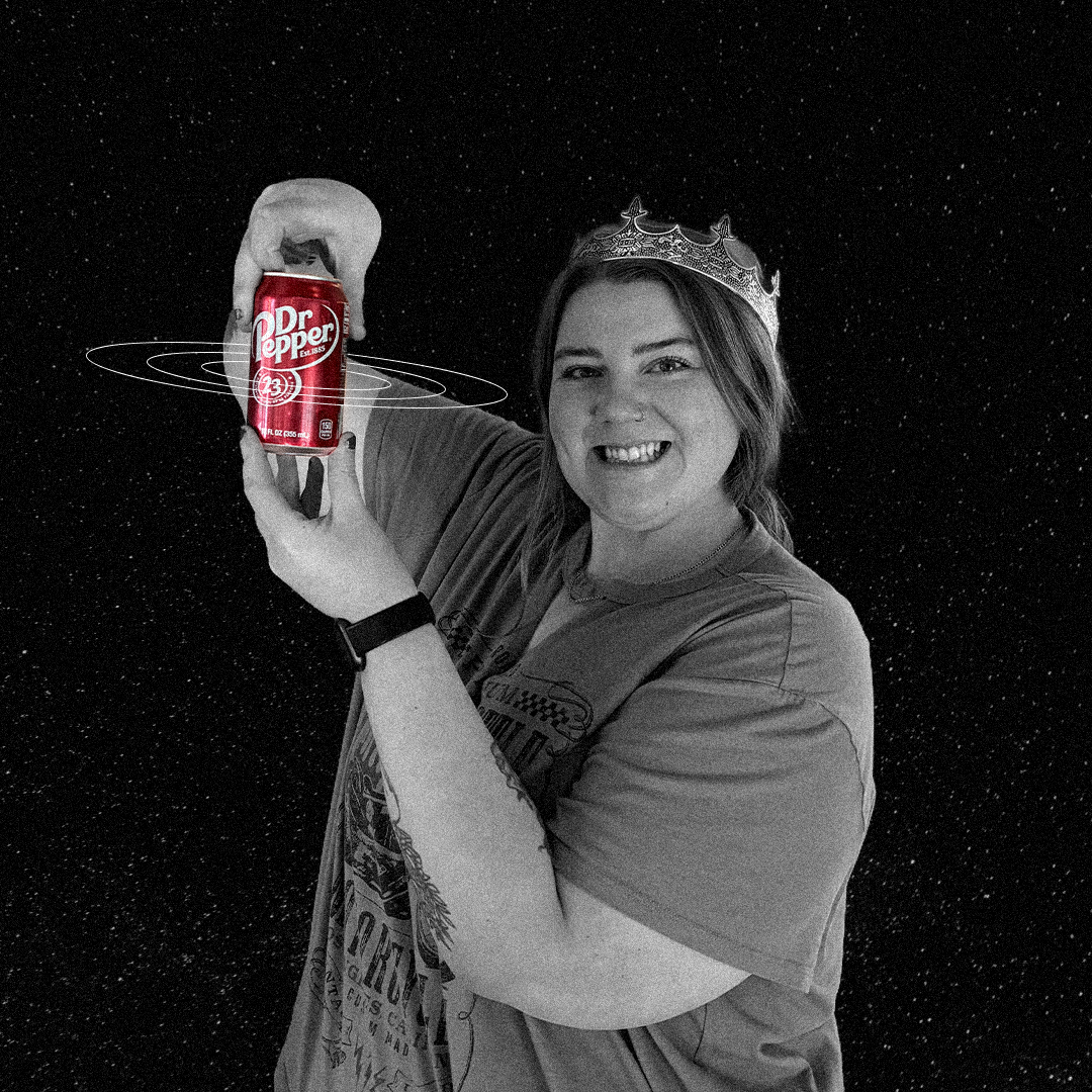 Smiling young man holds a large camera, points finger. He wears a tie-dye hoodie against a speckled black background.