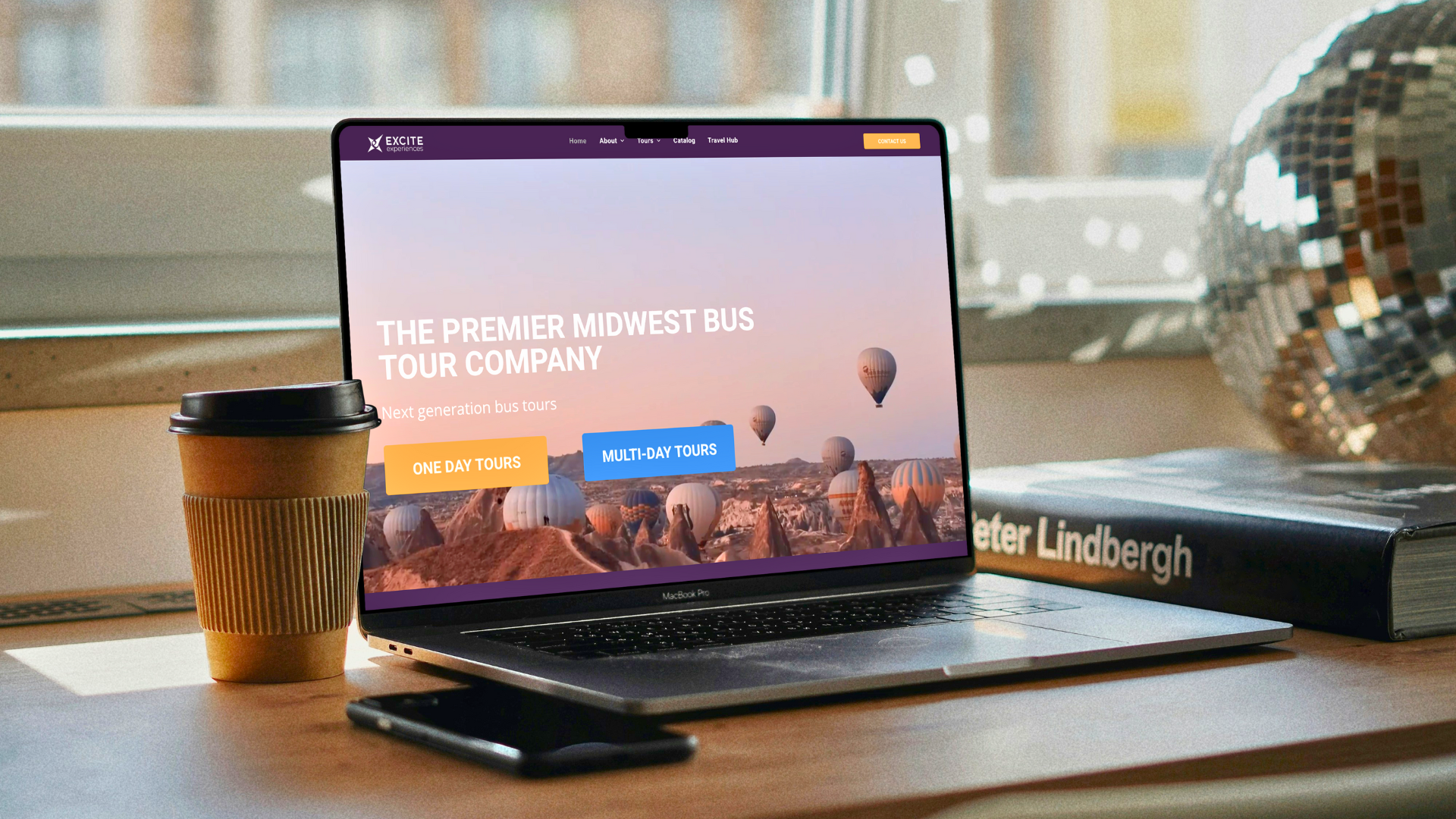 Laptop displaying a tour company website with a coffee cup and phone on a desk.