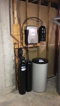 A water softener is sitting in a basement next to a wall.