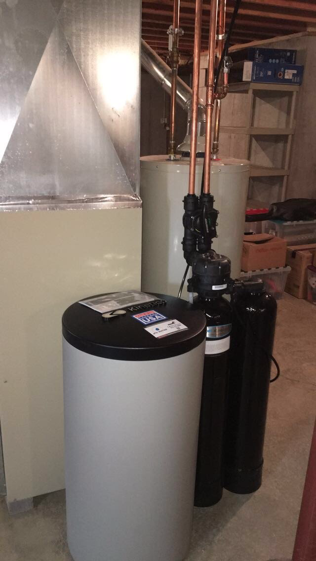 A water softener is sitting in a basement next to a water heater.