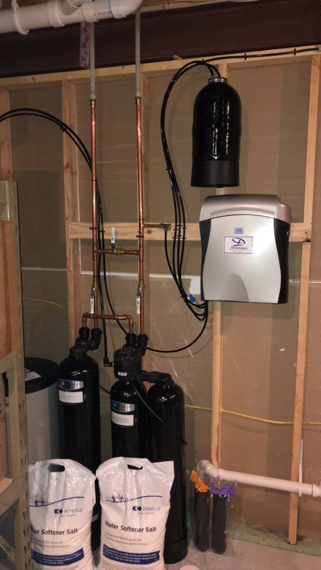 A room with a lot of pipes and a water softener on the wall.