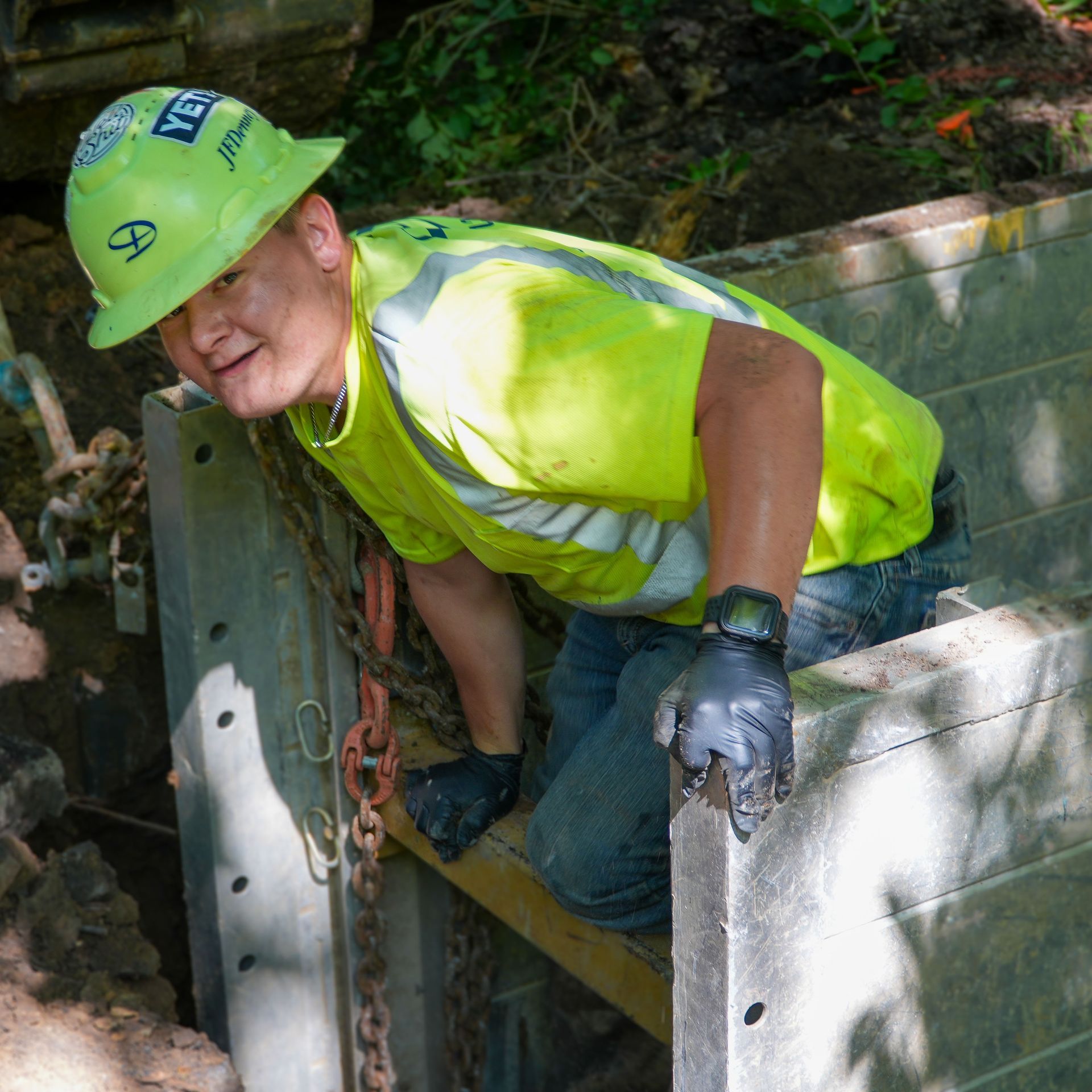 A man wearing a yellow shirt and a hard hat crawling out of a hole