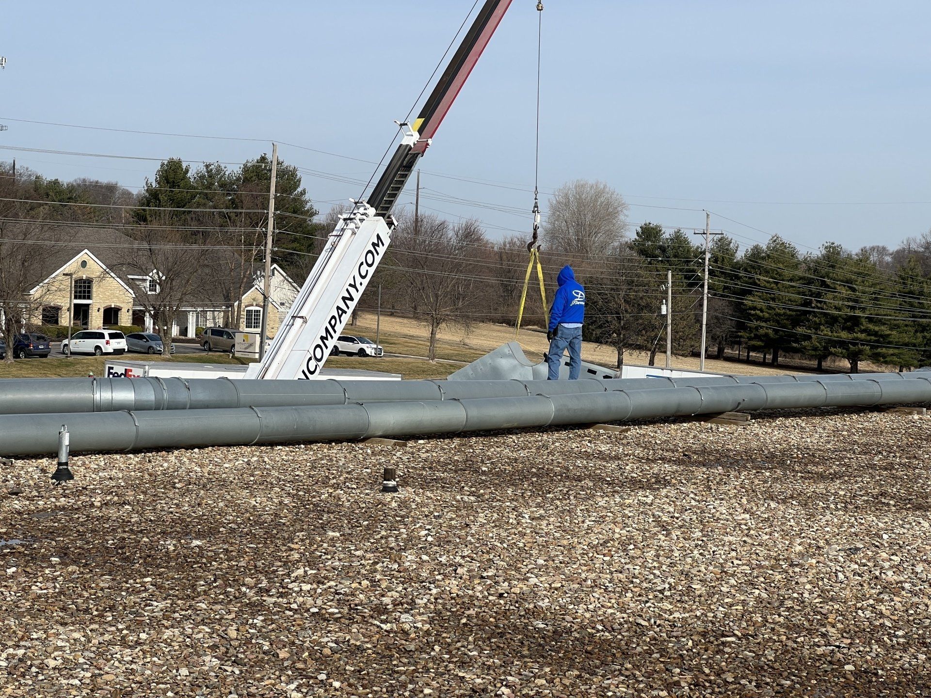 A crane is lifting a large metal pipe in a field.