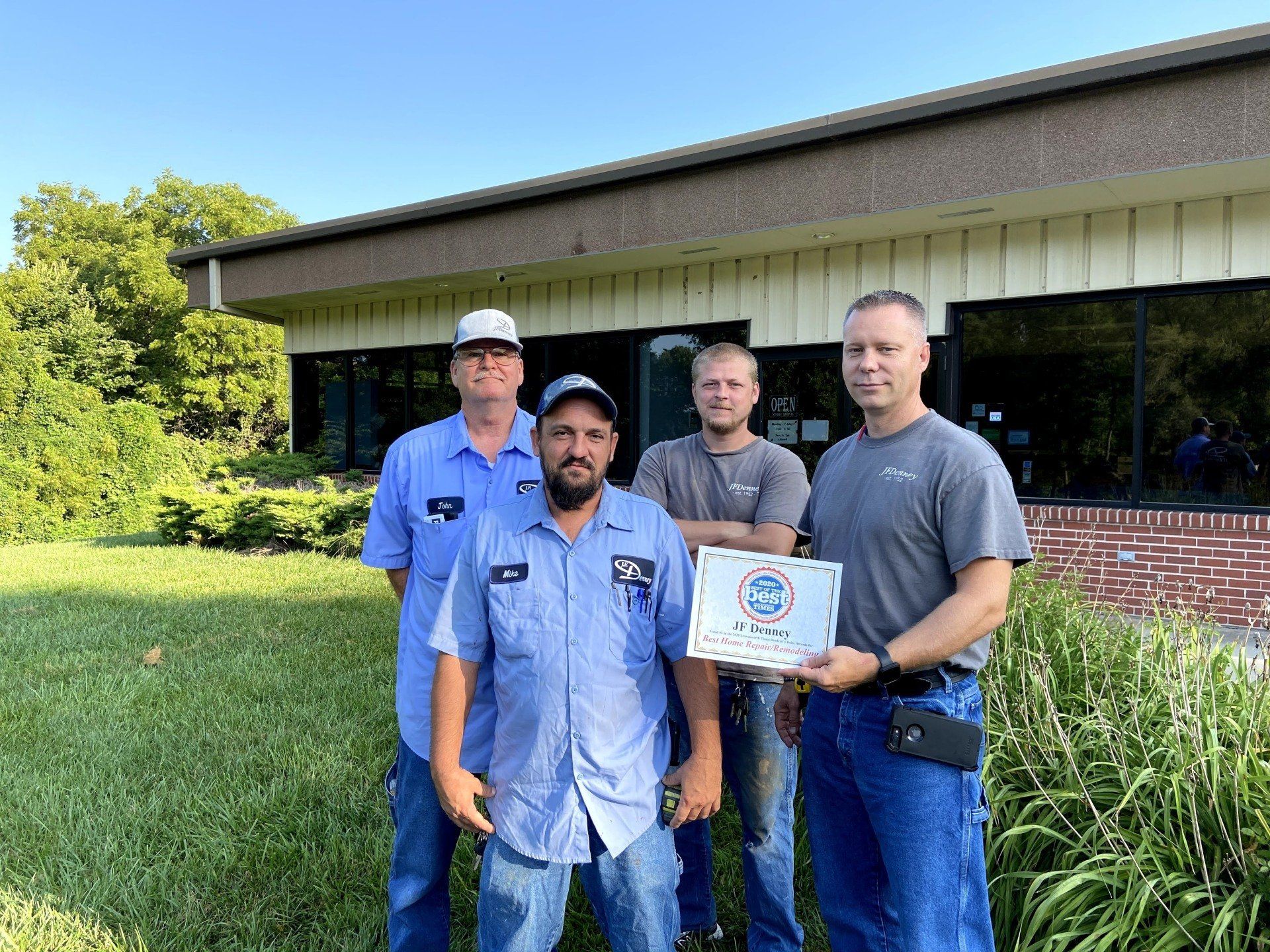 A group of men are standing in front of a building holding a certificate.