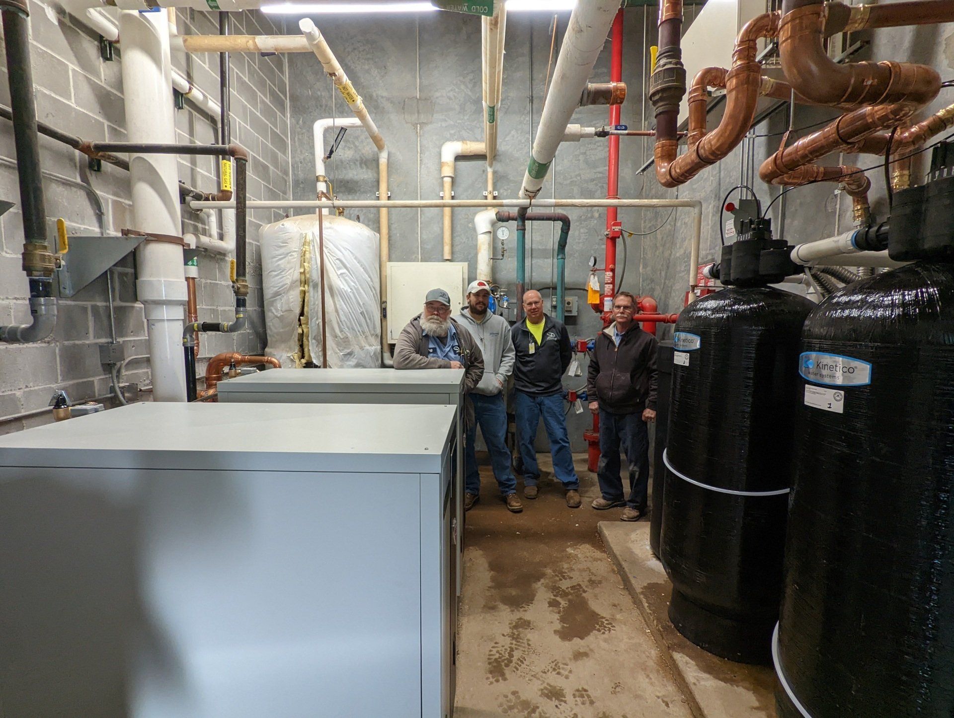 A group of men are standing in a room with pipes and tanks.