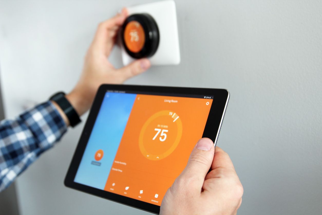 Hand holding a tablet to control a smart thermostat